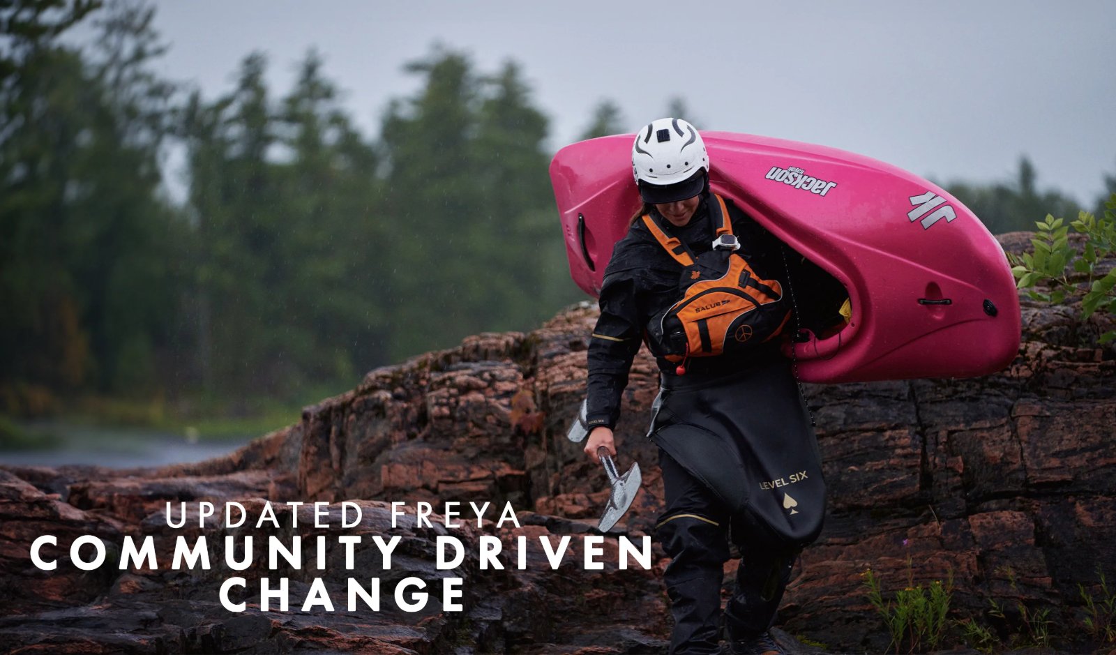 Level Six banner UPDATED FREYA COMMUNITY DRIVEN CHANGE: a paddler carries a bright pink kayak across wet rock in the rain