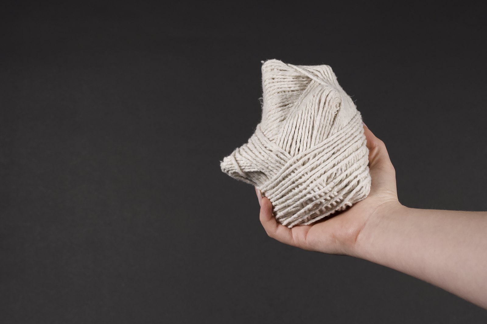SCENTLINK — woven scent object held in the hand against a dark ground